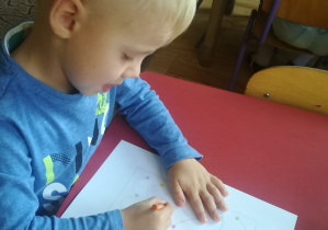 Chłopiec wykonuje pracę plastyczno-techniczną z kolorowych kropek